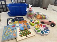 Toddler toys and books arranged on a table including colorful bath toys, wooden race car, Fisher Price game remote, ring stacker, and five children's books.