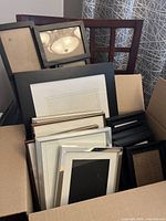13 various picture frames in box, showing assorted sizes and colors including black, white, silver, and brown.