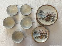 Top view of 5 vintage teacups placed upside down and 2 plates showing painted geisha scene and gold trim.