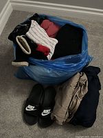 Lot of women’s clothing packed in a blue bag with some items visible including Nike slides and various jackets.
