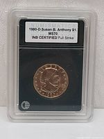 Front of coin encapsulated in hard plastic holder with certification label displaying 1980-D Susan B. Anthony $1 coin graded MS70 by INB.