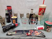 Overview of vintage Coca-Cola items including bottles, glasses, containers, and decorative pieces arranged on a table.