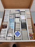 Top view of open box containing multiple stacks of hockey cards divided into sections with one visible BIEAF pin