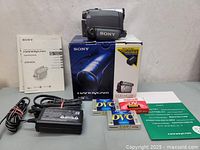 Full lot contents including camcorder, box, power adapter, power cable, MiniDV tapes, and user manuals arranged on a surface for display.