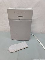 Front view of white Bose SoundTouch 10 wireless speaker with remote placed in front of it on a gray surface.