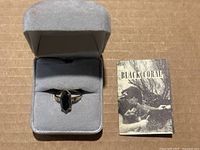 Ring displayed in gray jewelry box alongside Black Coral booklet