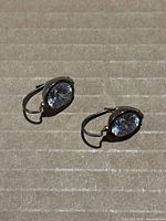 Pair of oval-shaped earrings showcasing clear round stones in bezel settings on a cardboard surface.