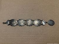 Full view of the antique bracelet laid flat showing all connected embossed panels with varied designs including floral and human portrait.