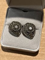Close-up image of front side of heart-shaped antique sterling silver earrings with marcasite and central gemstone in a grey velvet-lined jewelry box.