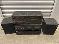 Full stack of JVC and Sony electronic audio components with two black Charleton speakers on either side on a concrete floor.