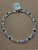 Gold-tone collar necklace laid flat on cardboard background showing full necklace shape, clear pavé crystals and colored stones.