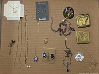 Overview of lot on cardboard showing all jewelry pieces spread out including necklace chains, earrings on card, brooch, cufflinks, decorative boxes, and large crystal piece.