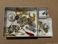 Overview of the full jewelry lot including brooches, pins, ring, and necklace shown inside a white box with velvet lining.