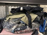 Photo of pile of men's dress shirts in assorted colors and patterns, some wrapped in plastic bags and some with tags.