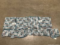 Full layout of the towel set on floor showing multiple folded towels with a rectangular geometric pattern in blue, gray, white.