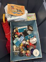 Overall lot view showing collectible dolls, blue box with mixed items, a red pouch, decorative cards, and packaging material.