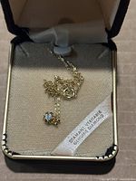 Close-up photo of a gold-tone chain necklace with a small clear stone pendant inside a beige velvet lined jewelry box.