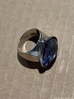 Angled front view of ring on cardboard showing band and purple stone