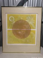 Full view of the framed artwork showing the abstract print with dominant yellow and brown circular elements.