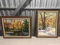Two framed oil paintings side by side. Left painting shows autumn pond scene, right painting shows snowy trees scene.