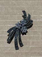Front view showing silver-tone brooch with marcasite and clear stones arranged in ribbon and floral design.