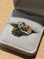 Ring in gray jewelry box showing wrap-around design with two cat heads: one polished, one pave-set with clear and black crystals.