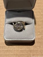 Front view of the vintage sterling silver ring with a clear round stone in bezel setting, displayed in a grey ring box.