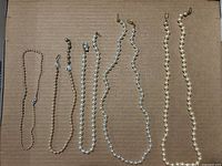 Overview of all seven necklaces laid out on cardboard