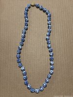 Full view of vintage Chinese cobalt blue and white porcelain bead necklace with gold-tone clasp laid flat on a cardboard background