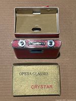 Top view of vintage Crystar opera glasses with original box. Shows red textured body and box with 'OPERA GLASSES CRYSTAR' text.