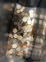 Photo showing a collection of mixed world coins inside a container, displaying different sizes and metal types.