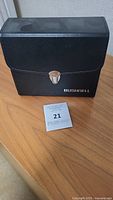Black carrying case embossed with Bushnell logo on wooden surface with auction tag.