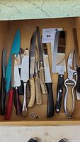 Overview of all knives, scissors, and peeler inside a drawer showing their variety and condition.