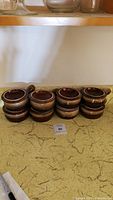 Eight stacked brown ceramic French onion soup crock bowls with matching lids displayed on countertop.