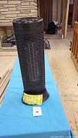 Front view of Honeywell black tower heater on blue cloth showing vertical grill and overall shape.