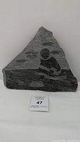 Front view of triangular granite stone artwork with carved Inuit figure and auction lot number label.