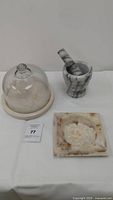 Photo shows a glass dome on a round marble base, a marble mortar with pestle, and a square marble tray with natural veining.