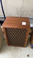 Front view of one speaker showing wood veneer cabinet and lattice grille