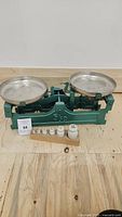 Full view of the vintage green balance scale with two round metal pans and set of white weights on a wooden base.