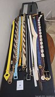 Full view of 12 vintage belts laid out flat showing various styles, colors, and buckle designs.