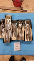 Set of assorted forks, knives and spoons arranged in original cardboard boxes on blue fabric.