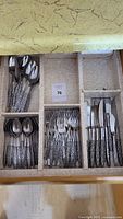 Drawer with cutlery set including spoons, forks, and knives with decorative handles.