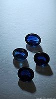 Four oval cut royal blue sapphires laid out on a light surface, showing deep color and faceting.