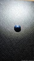 Close-up image of a blue star sapphire oval cabochon showing six-ray star asterism effect on a textured black surface.