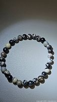 Photo of a natural black web jasper bracelet with round beads on a neutral surface showing the distinctive black and white web-like patterns of the stones.