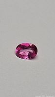 Oval cut hot pink topaz gemstone photographed from above on light surface showing color and cut.
