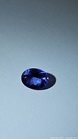 Close-up photo of one natural oval cut deep purple-blue tanzanite gemstone showing oval shape and faceting reflective surface.