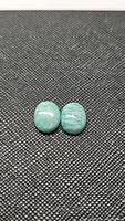 Two polished amazonite cabochon gemstones placed side by side on textured black surface, showing their size, color, and pattern.