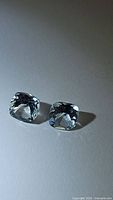 Pair of cushion cut light baby blue topaz gemstones placed side by side on white surface, showing shape, color, and size.