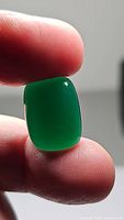 Close-up of green onyx gemstone showing color and cushion cabochon shape held between fingers with natural light highlighting translucency and shine.